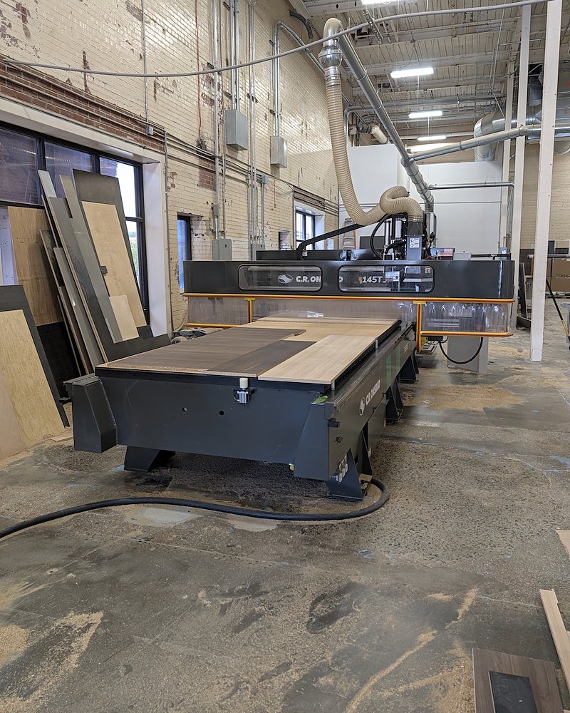 CNC router with a sheet of dark and light wood-grain parts on the bed