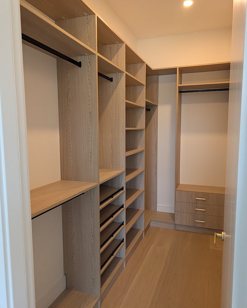 Walk-in closet in light wood-grain laminate with rods, shelving, and shoe storage