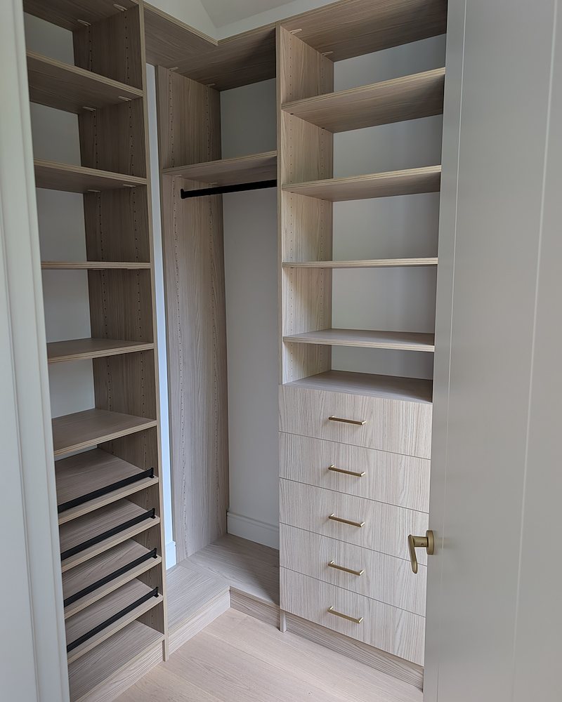 Corner closet in light wood-grain laminate with brass pulls and pull-out shoe shelves
