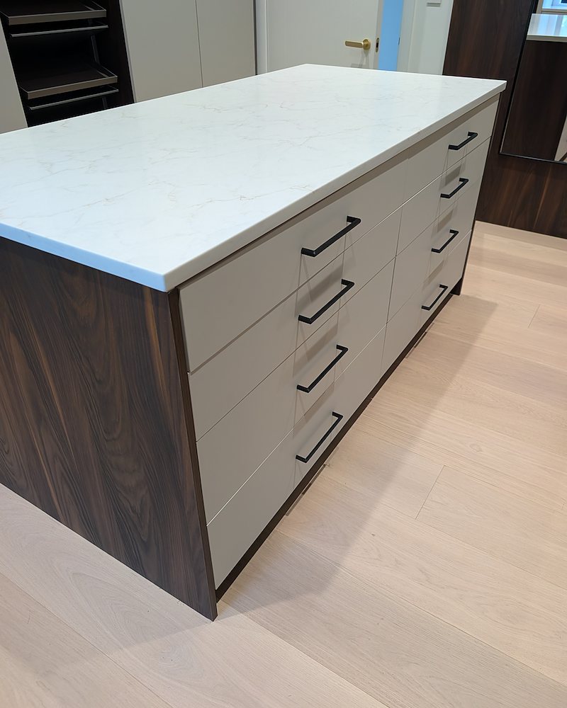 Freestanding island in a walk-in closet, with light drawer fronts on both long sides, dark wood-grain laminate end panels, and a white top