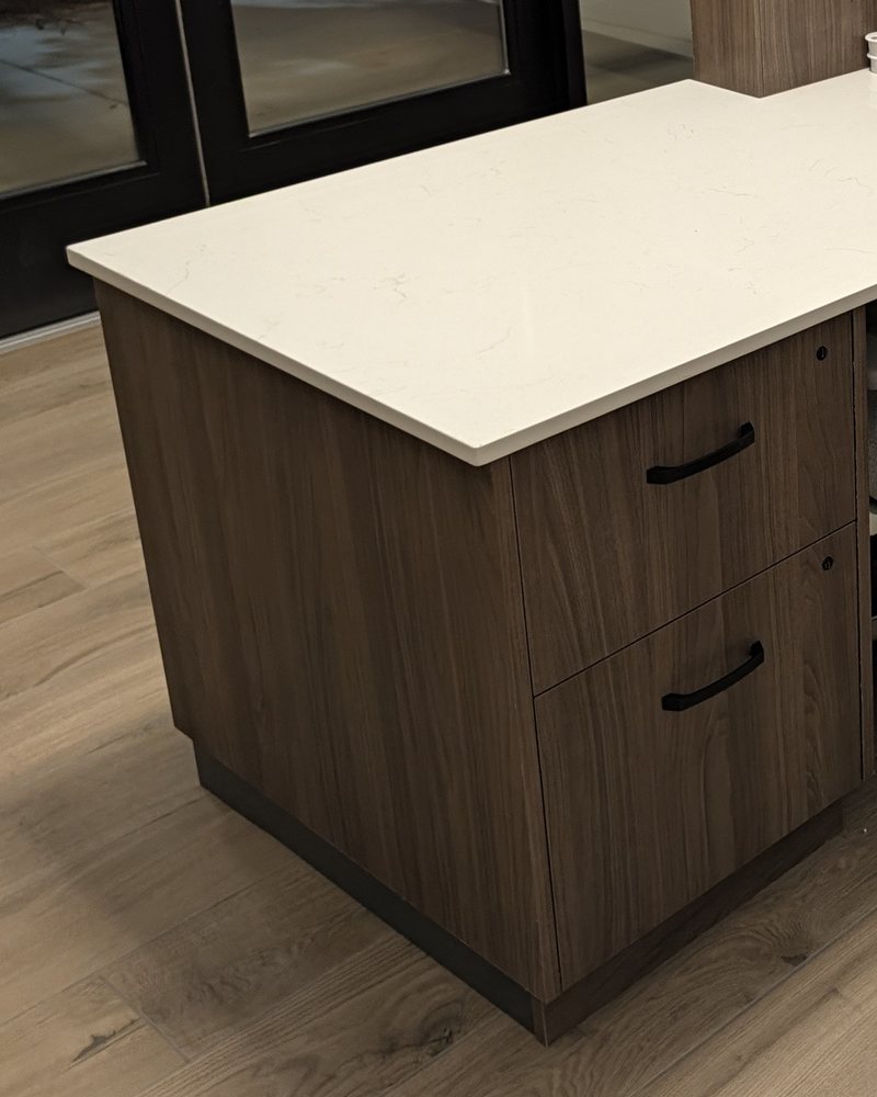 End of a reception desk: a two-drawer locking pedestal in dark wood-grain laminate under a quartz top