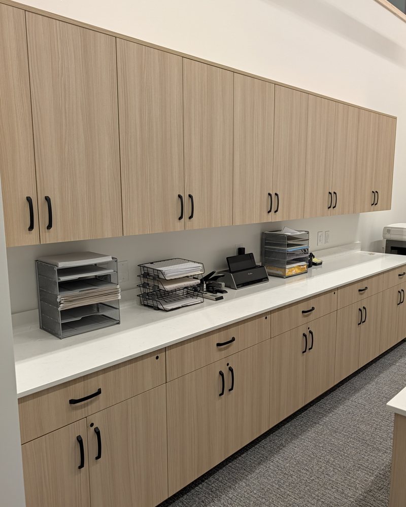 Office workroom: a full wall of light wood-grain laminate upper cabinets over drawer and door bases, quartz top