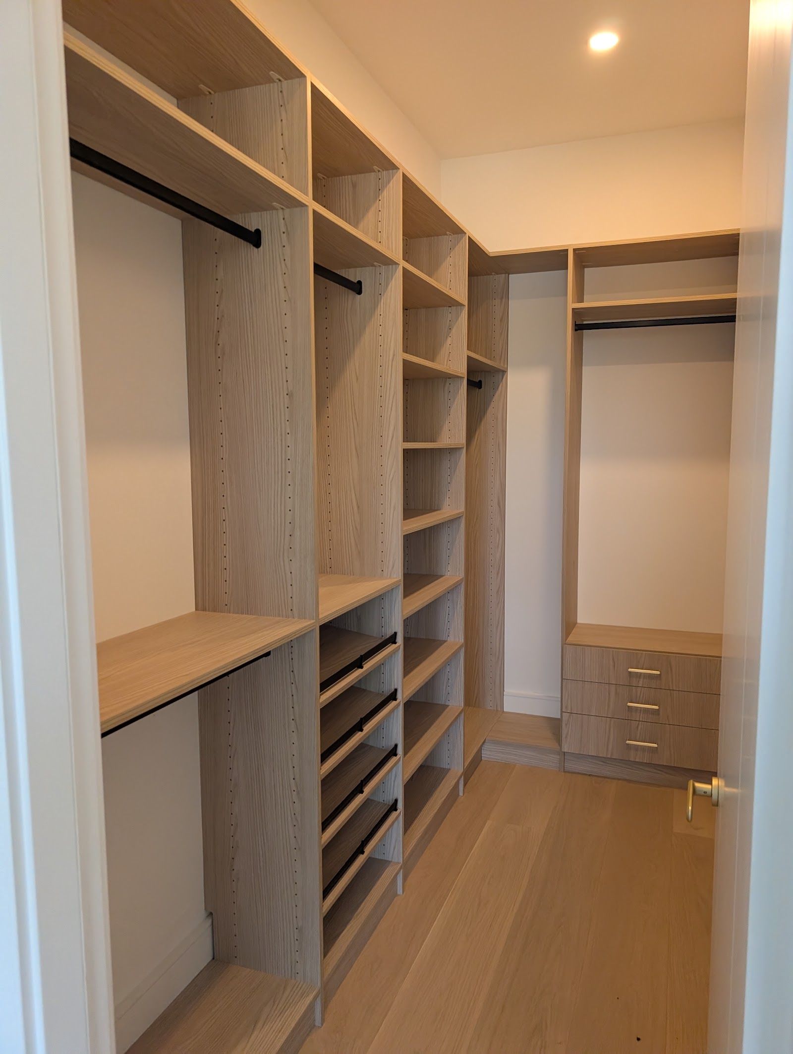 Light oak walk-in closet system with rods, shelving, and shoe storage