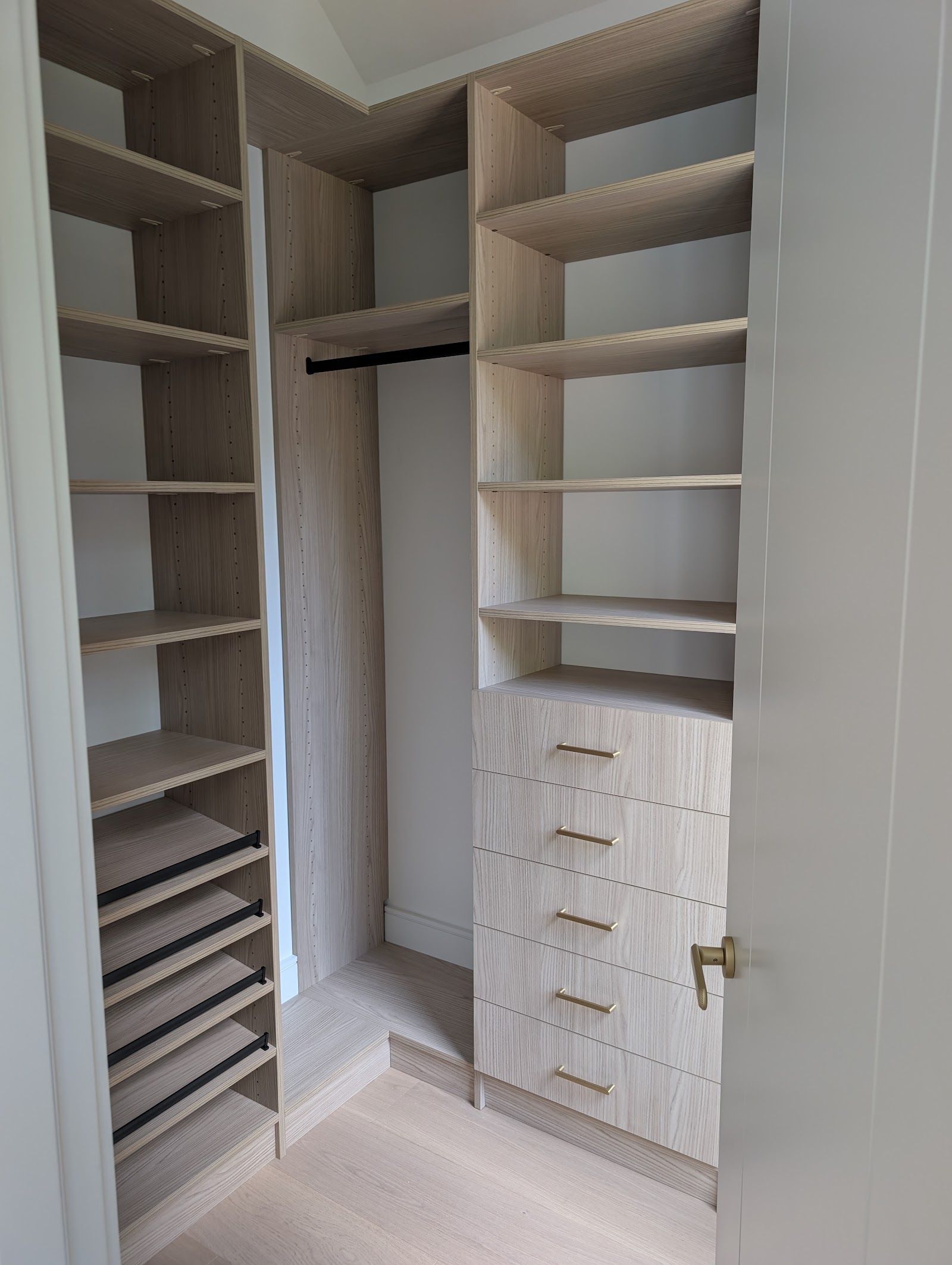 Light oak corner closet with brass pulls and pull-out shoe shelves